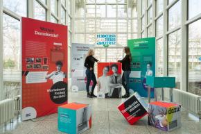 Zwei Frauen stehen in der Ausstellung mit Info-Stelen und Würfeln.