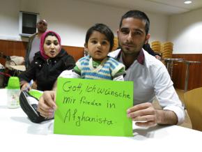 Ein Vater und ein kleines Kind sitzen an einem Tisch und halten ein Schild mit der Aufschrift "Gott, ich wünsche mir frieden in Afghanistan".
